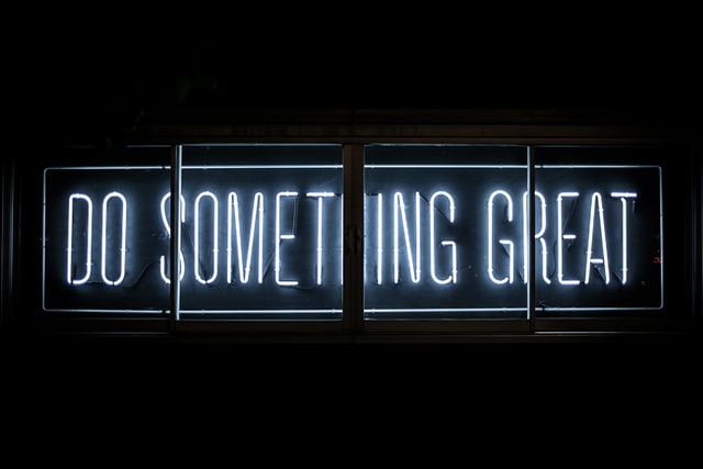 A neon sign reading Do Something Great against a black background