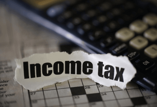 A ripped piece of paper with "Income tax" on a crossword puzzle and calculator