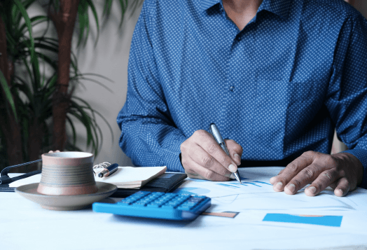 Person in blue shirt writing on document, calculator, coffee cup