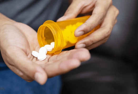 Hands pouring white pills from an orange bottle