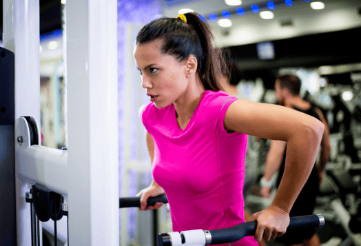 Woman in pink shirt doing dips on gym equipment