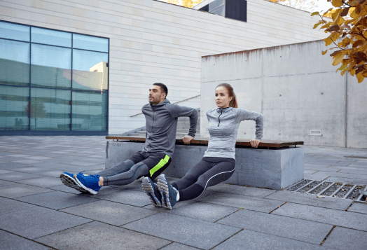 Man and woman doing triceps dips on a bench outdoors