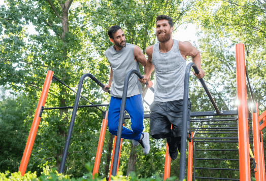Two men doing parallel bar dips outdoors, smiling